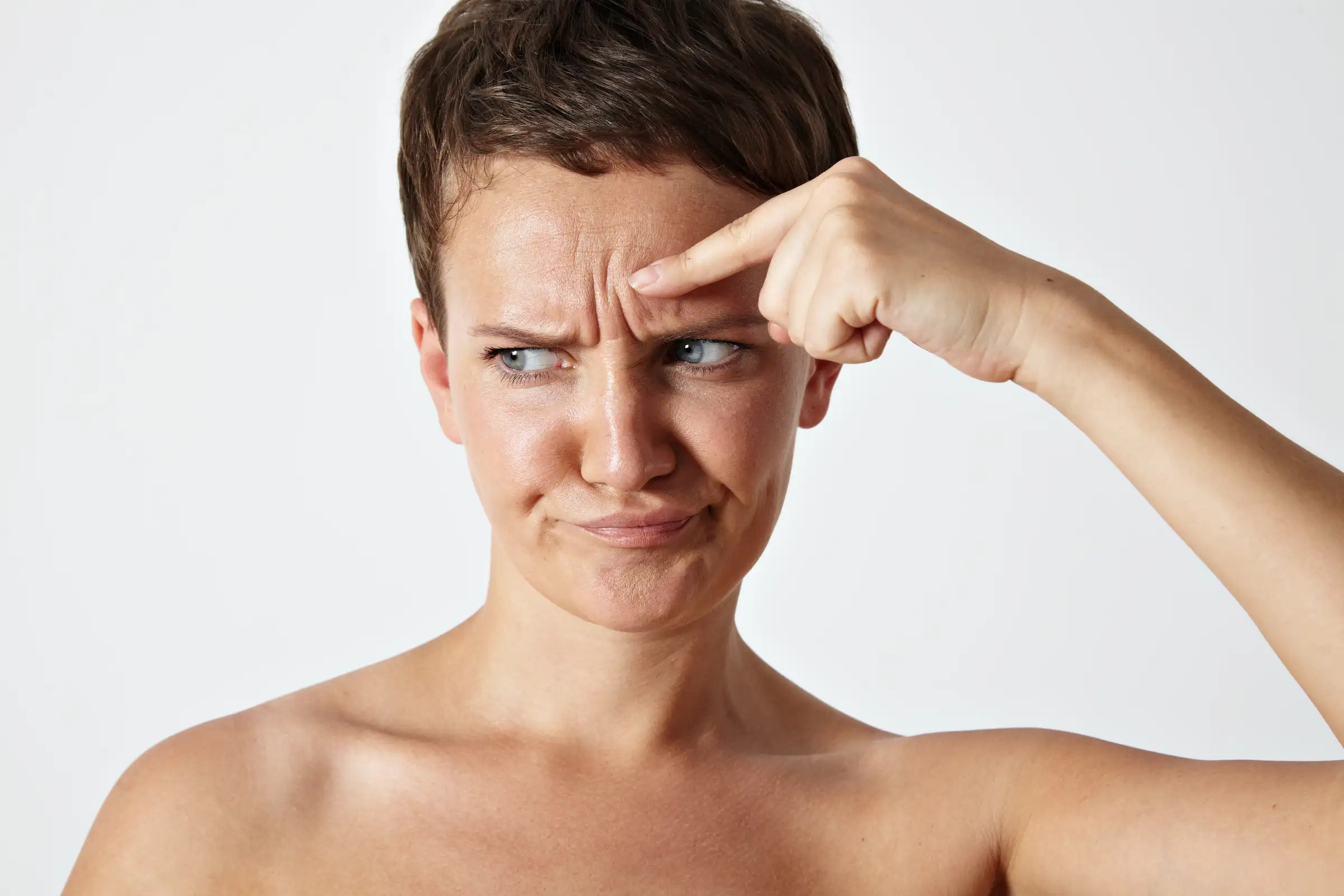 A woman examining forehead wrinkles before a consultation botox vs dermal fillers treatment at Skincare Sommelier Beauty Lab & Med Spa in NYC.