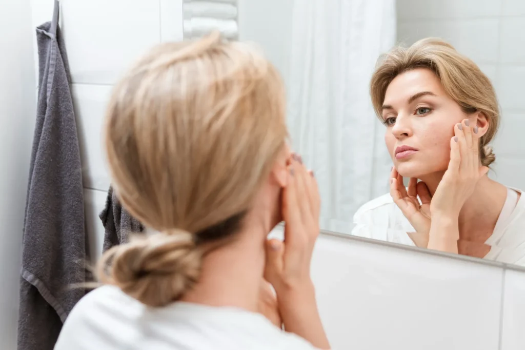 A woman checking her facial filler results in a mirror, following the day-by-day recovery timeline after a visit to a NYC med spa.