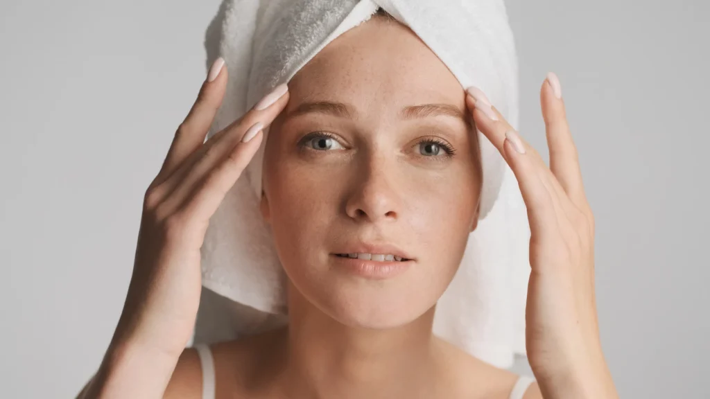 A woman examining her smooth and healthy facial skin, illustrating how to avoid Sculptra nodules and granulomas with expert care.