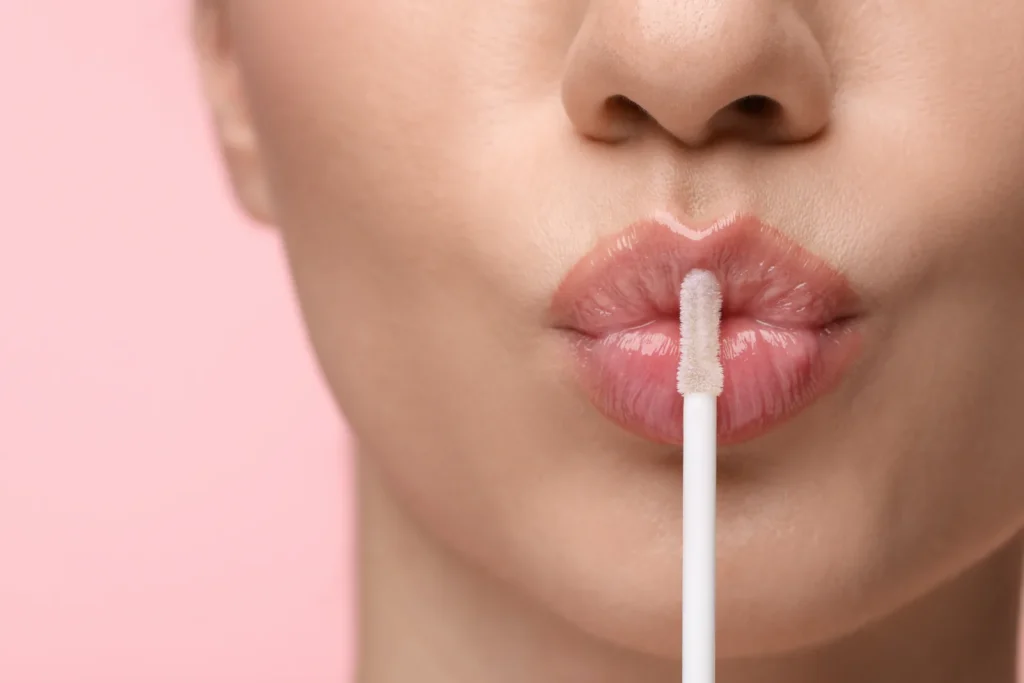 Close-up of glossy lips during lip filler aftercare on a pink background