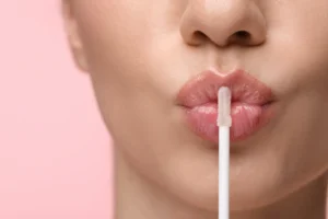 Close-up of glossy lips during lip filler aftercare on a pink background