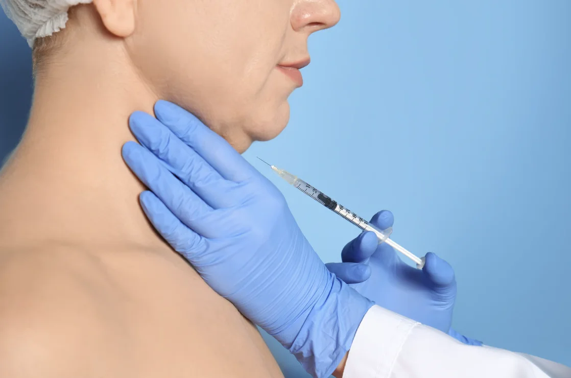 Injector in blue gloves giving a Kybella injection under the chin to reduce a double chin, Kybella treatment in Forest Hills, NY.